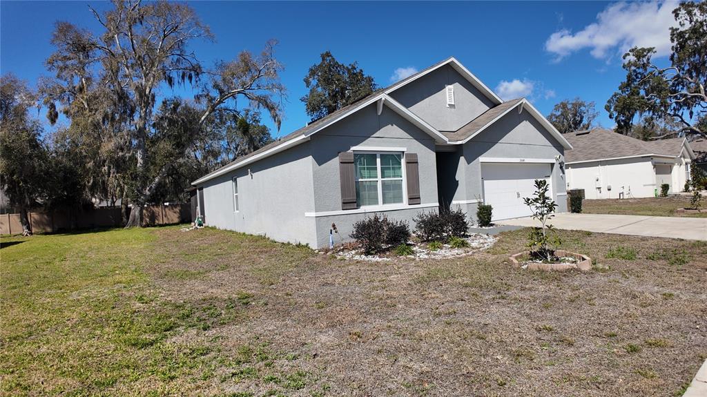 A gray single-story house with a two-car garage and a large, grassy front yard — 35045 SWEET LEAF LANE, LEESBURG, FL