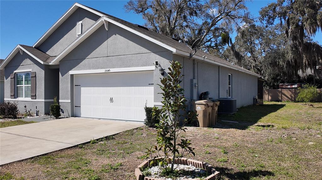 A gray single-story house with a two-car garage and a small tree in front — 35045 SWEET LEAF LANE, LEESBURG, FL