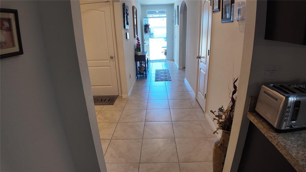 A tiled hallway leads to an open front door, flanked by interior doors and decor — 35045 SWEET LEAF LANE, LEESBURG, FL