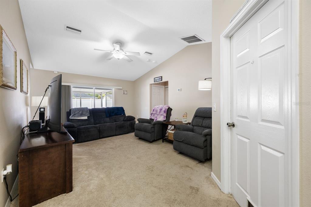 A living room with a vaulted ceiling, carpeted floors, a dark sofa, and two armchairs — 2802 93RD COURT E, PALMETTO, FL