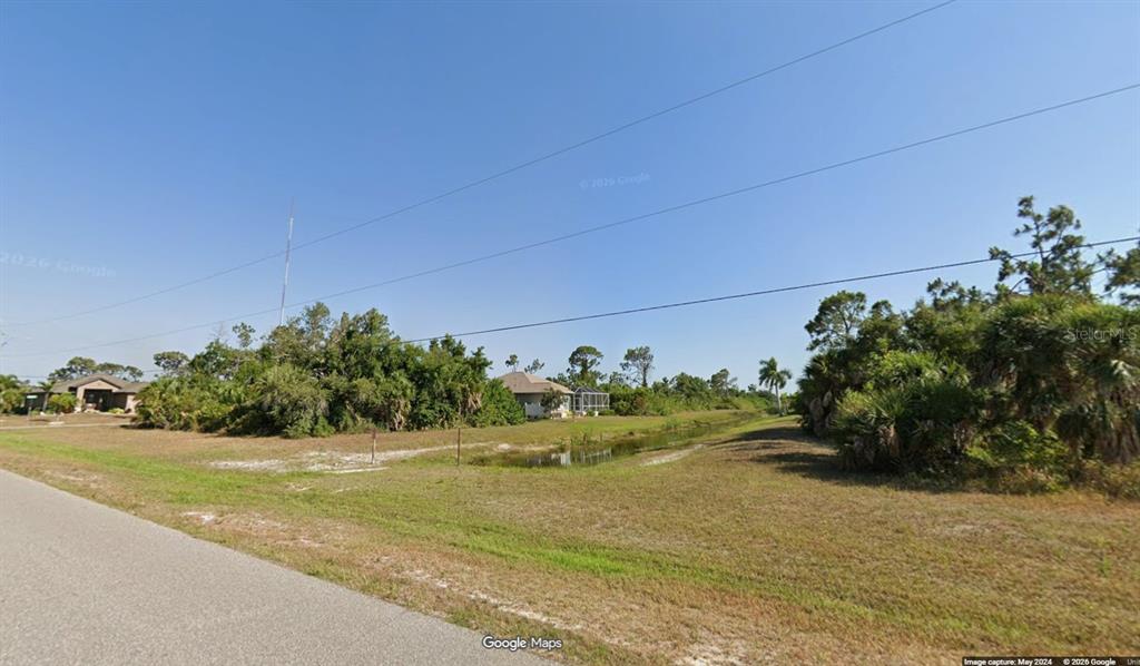 A vacant grassy lot with a small drainage ditch and surrounding trees under a clear sky — 155 APOLLO DRIVE, ROTONDA WEST, FL