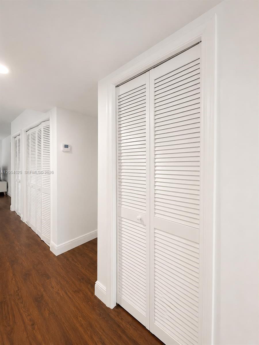 A hallway features white louvered closet doors and dark wood-look flooring — 16571 Blatt Blvd # 203, Weston FL 33326, WESTON, FL