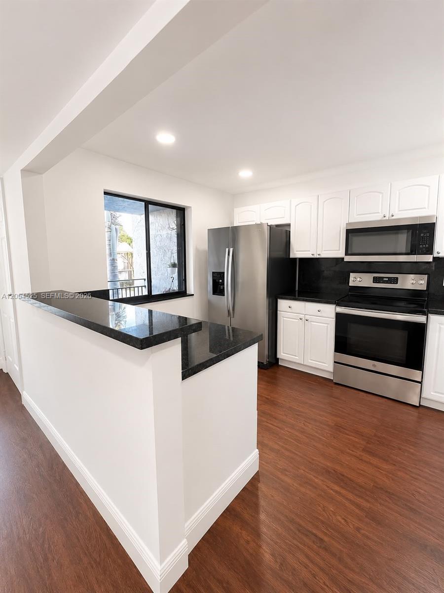A kitchen features white cabinets, black granite countertops, stainless steel appliances, and wood-look flooring — 16571 Blatt Blvd # 203, Weston FL 33326, WESTON, FL