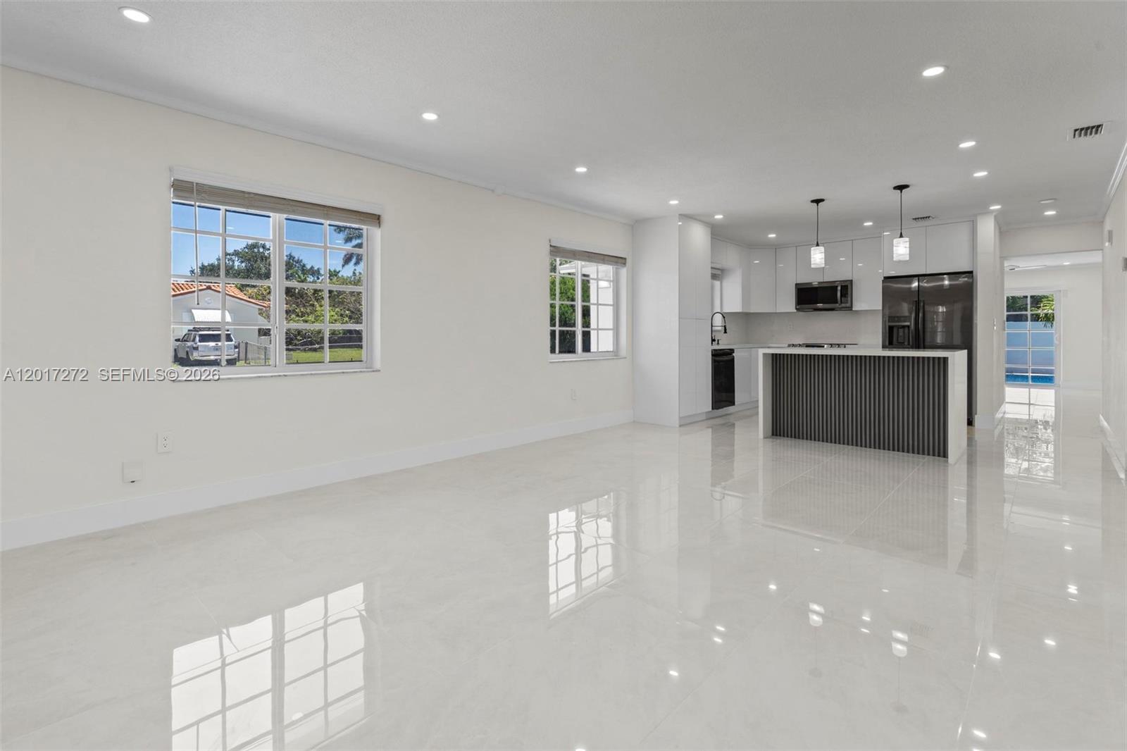 A bright, open-concept kitchen and living area features white cabinetry, a dark island, and tile flooring — 1900 SW 24th St, Miami FL 33145, MIAMI, FL