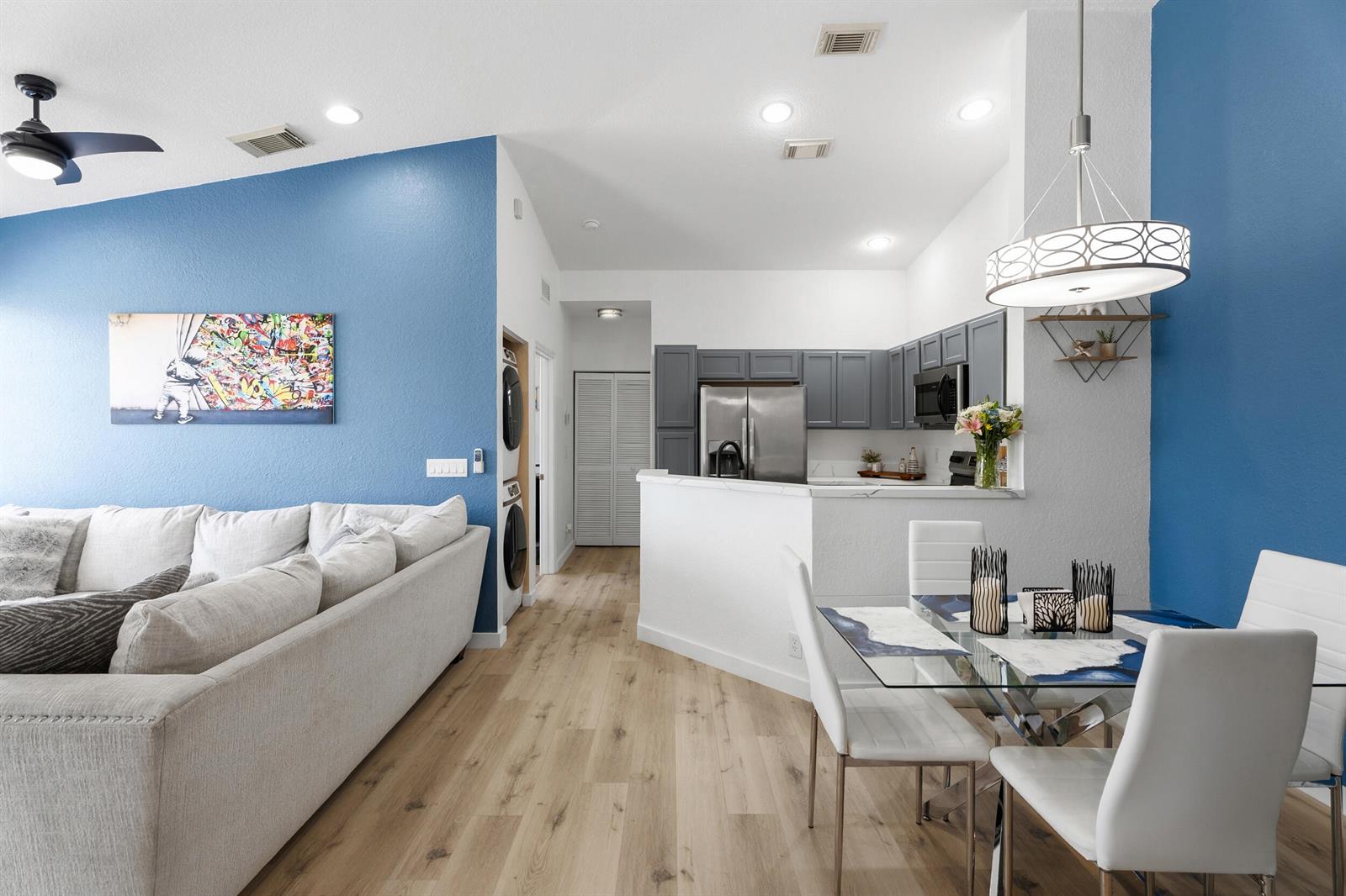 A living room and dining area feature blue accent walls, gray cabinets, and wood flooring — 1706 Carvelle Drive, Riviera Beach FL 33404, RIVIERA BEACH, FL