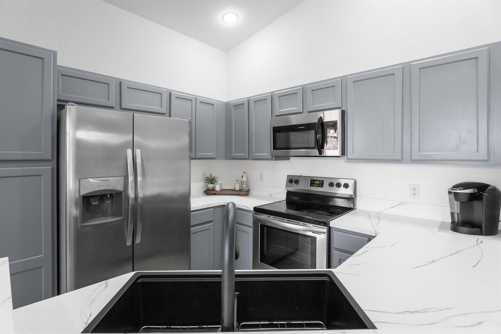 A kitchen features grey cabinets, stainless steel appliances, white marble-patterned countertops, and a black sink — 1706 Carvelle Drive, Riviera Beach FL 33404, RIVIERA BEACH, FL