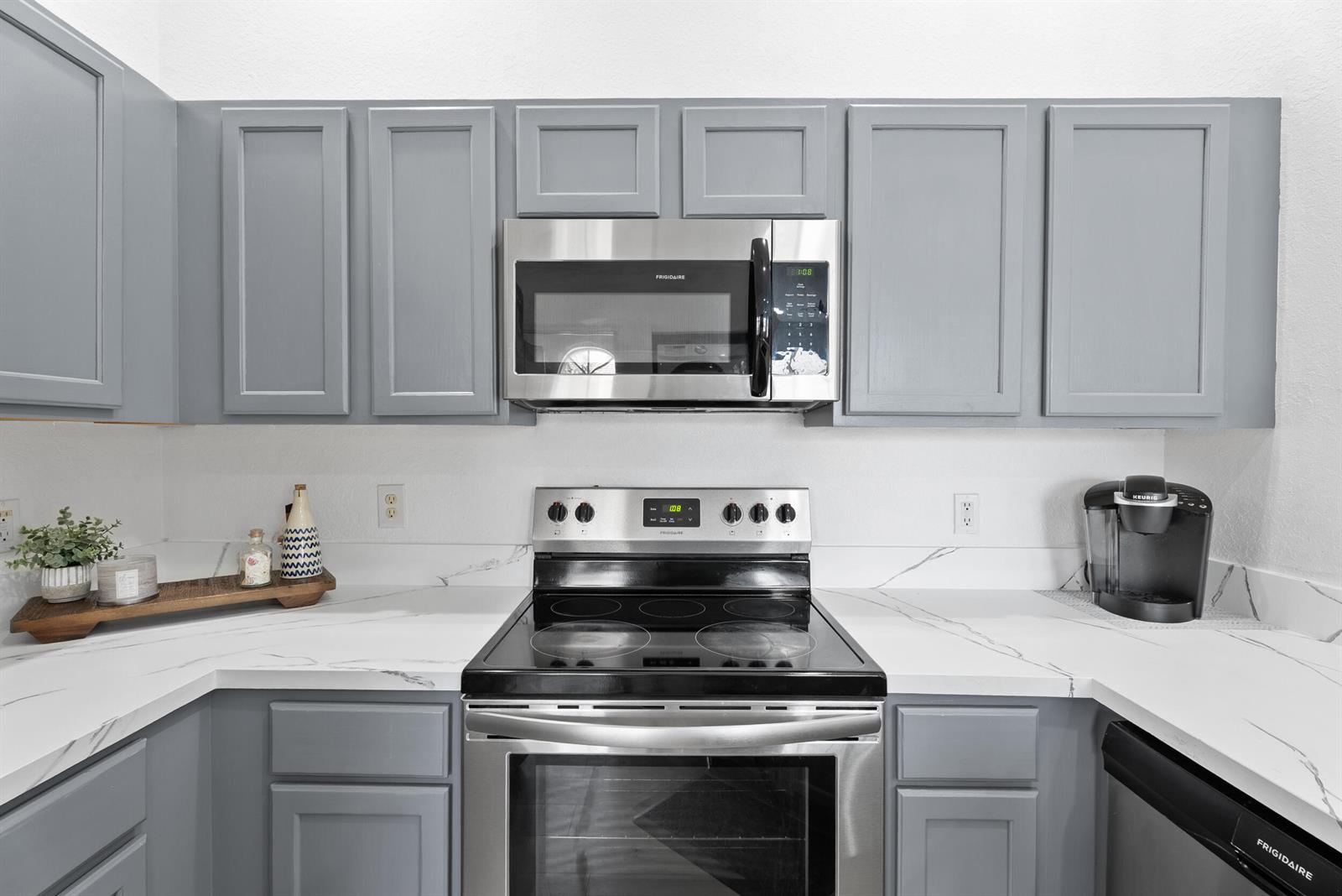 A kitchen features gray cabinets, stainless steel appliances, and white countertops with marble veining — 1706 Carvelle Drive, Riviera Beach FL 33404, RIVIERA BEACH, FL