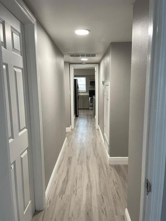A hallway with light-colored wood-look flooring leads to a kitchen with gray cabinets — 2302 CONTINENTAL BOULEVARD, ORLANDO, FL