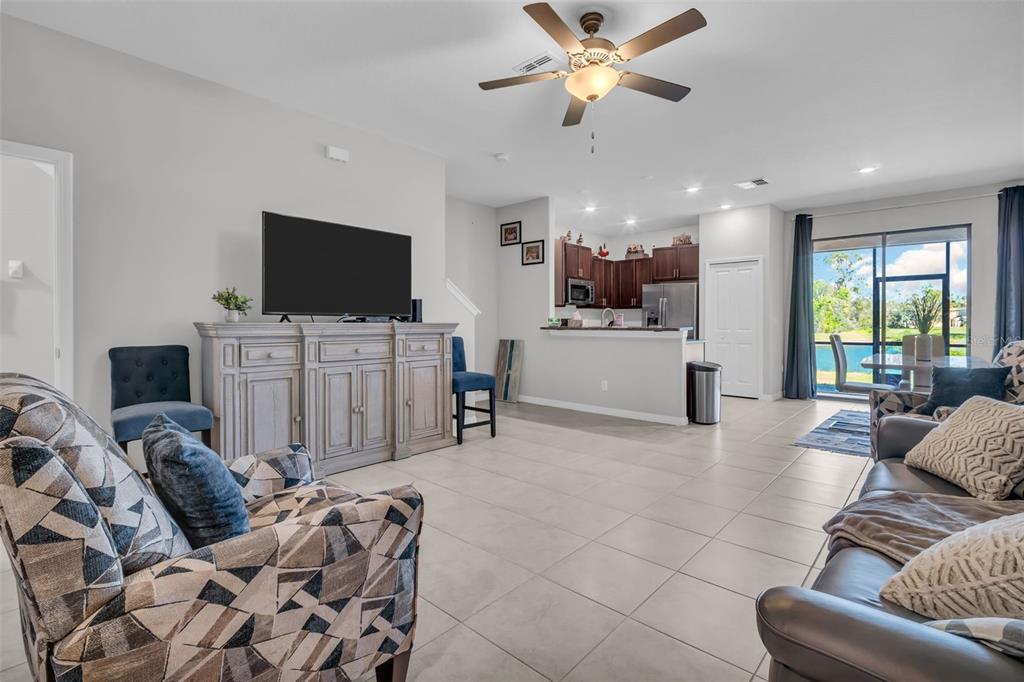 An open-concept living room and kitchen featuring tile flooring, a ceiling fan, and sliding doors — 8512 REEDVILLE STREET, NEW PORT RICHEY, FL