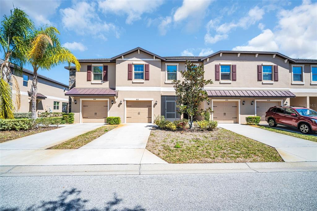 A row of two-story townhomes with beige stucco facades, brown garage doors, and concrete driveways — 8512 REEDVILLE STREET, NEW PORT RICHEY, FL