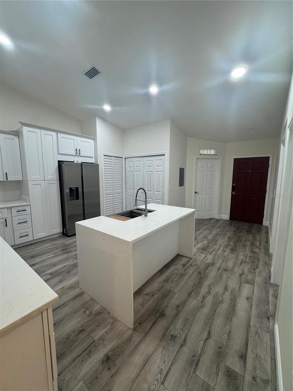 A modern kitchen features white cabinetry, a central island with a sink, and wood-look flooring — 2880 CLUB CORTILE CIRCLE UNIT B, KISSIMMEE, FL