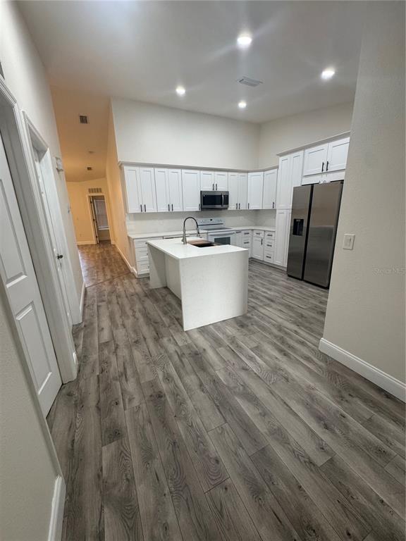 A kitchen features white cabinetry, a central island with a sink, and gray wood-look flooring — 2880 CLUB CORTILE CIRCLE UNIT B, KISSIMMEE, FL