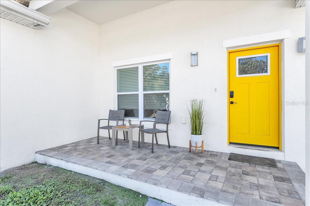 A paved front porch features two chairs, a small table, and a bright yellow door — 2402 W FIG STREET, TAMPA, FL