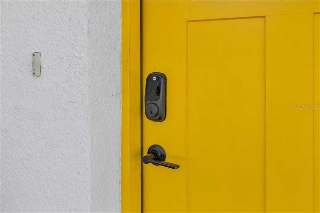 A bright yellow door with a black smart lock and handle is set against a white wall — 2402 W FIG STREET, TAMPA, FL