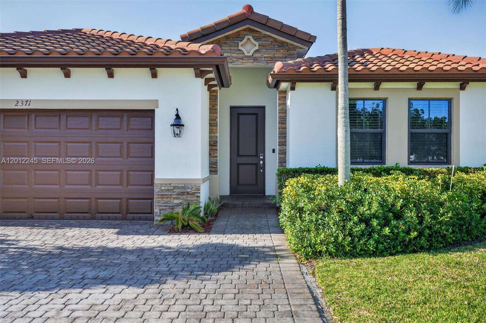 The exterior of a single-story house features a brown garage door, tiled roof, and entryway — 2371 SE 1st Ct, Homestead FL 33033, HOMESTEAD, FL