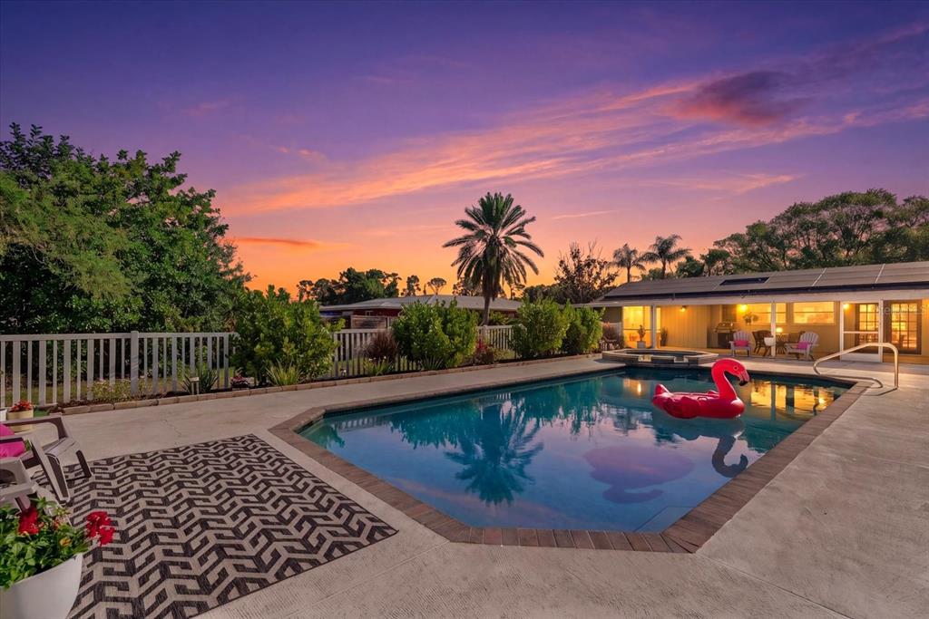 A backyard swimming pool with a pink flamingo float at sunset near a residential house — 5868 DENISON DRIVE, VENICE, FL