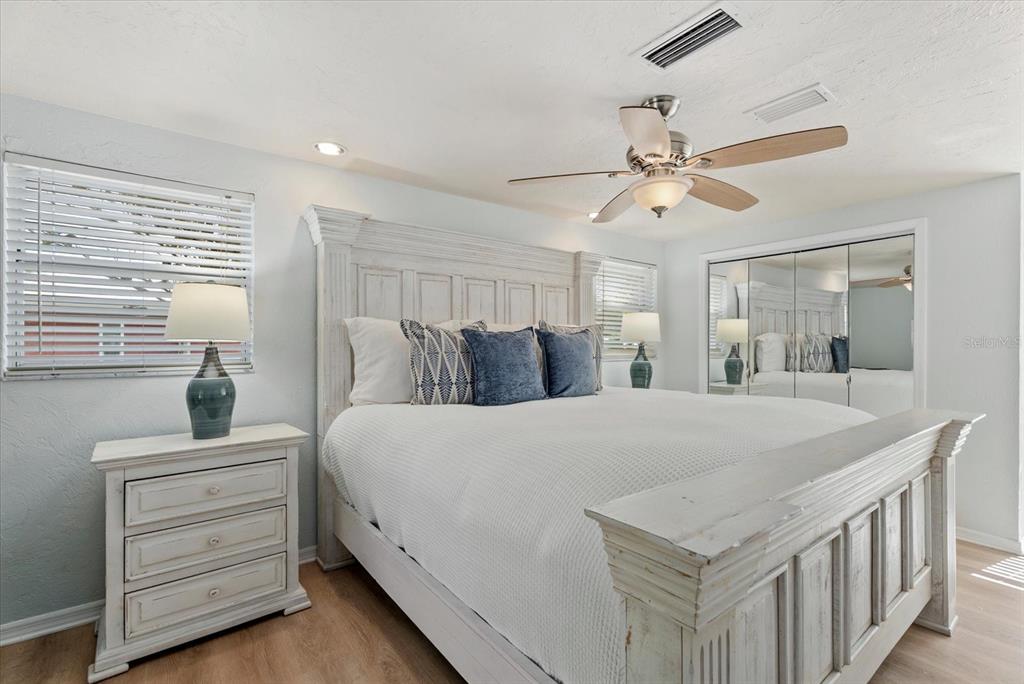 A bedroom features a white wooden bed frame, matching nightstand, and mirrored closet doors — 5868 DENISON DRIVE, VENICE, FL