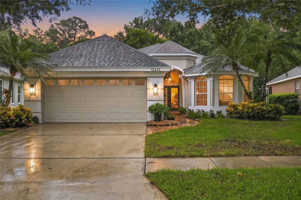 A single-story house with a beige garage and a front lawn under large trees — 10413 APPLECROSS LANE, TAMPA, FL
