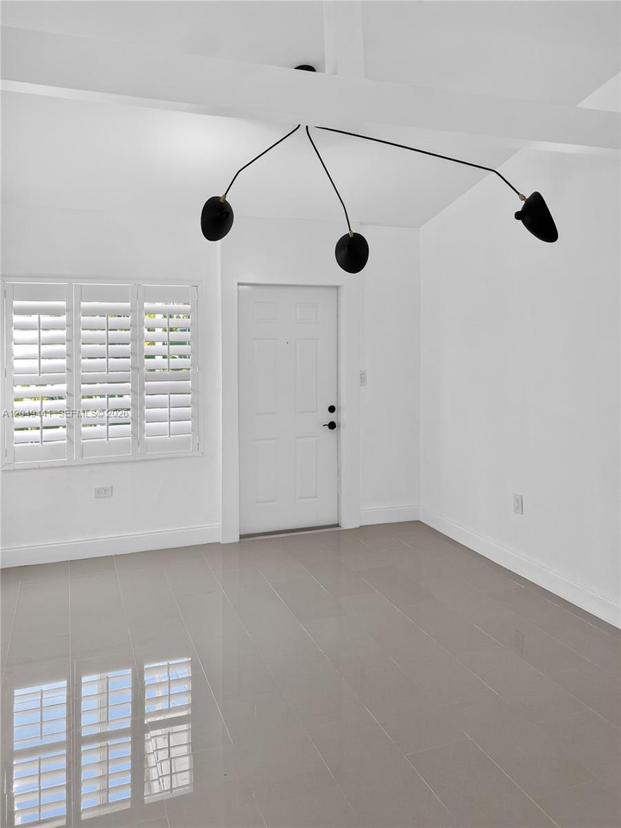 An empty room features white walls, light tile flooring, a white door, and a modern chandelier — 525 NE 63rd St # 4, Miami FL 33138, MIAMI, FL