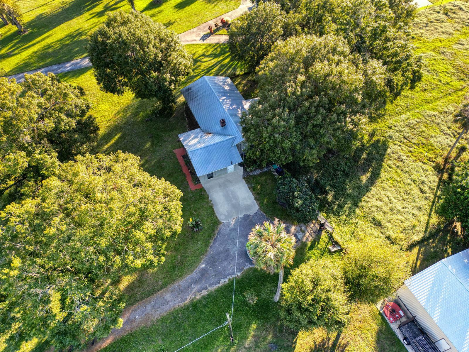 An aerial view shows a house with a metal roof surrounded by trees and grass — 1031 SW 24th Avenue, Okeechobee FL 34974, OKEECHOBEE, FL