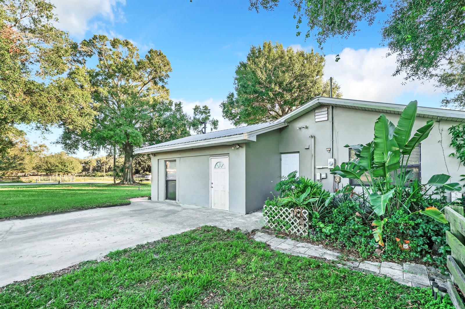 A single-story house with a concrete driveway, white doors, and lush landscaping under a sky — 1031 SW 24th Avenue, Okeechobee FL 34974, OKEECHOBEE, FL