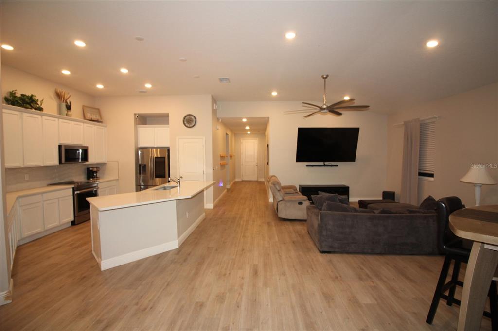 An open-concept kitchen and living area with white cabinets, light wood flooring, and a ceiling fan — 9449 SANDERS PARK PLACE, SEFFNER, FL