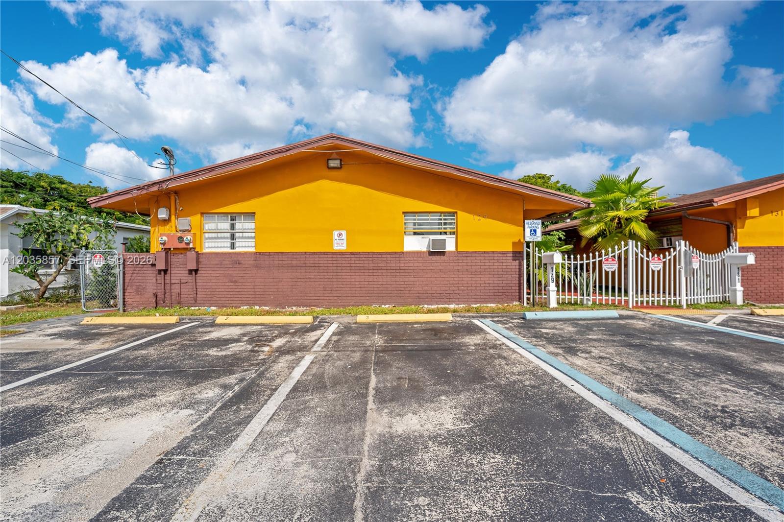 A yellow and brown single-story building features a parking lot with marked spaces — 129-131 SE 5th St, Hallandale Beach FL 33009, HALLANDALE BEACH, FL