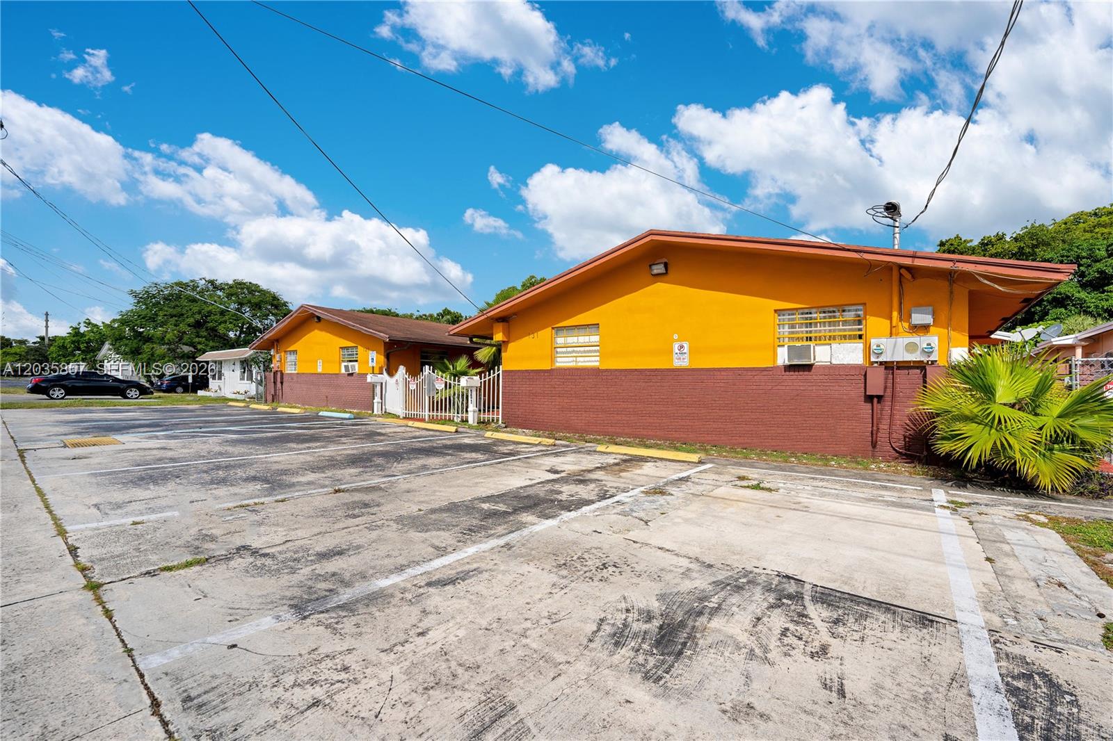 An exterior view of a yellow and brown building with an adjacent paved parking lot — 129-131 SE 5th St, Hallandale Beach FL 33009, HALLANDALE BEACH, FL