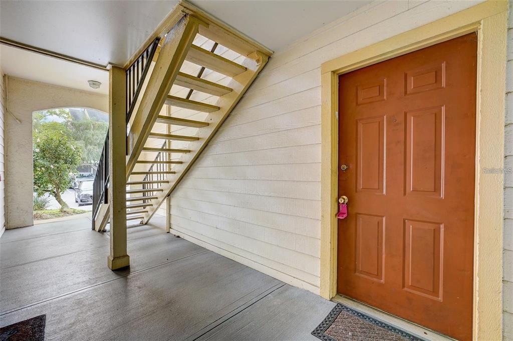 An exterior view of a covered porch featuring a staircase and a brown front door — 11901 4TH STREET N UNIT 10105, ST PETERSBURG, FL