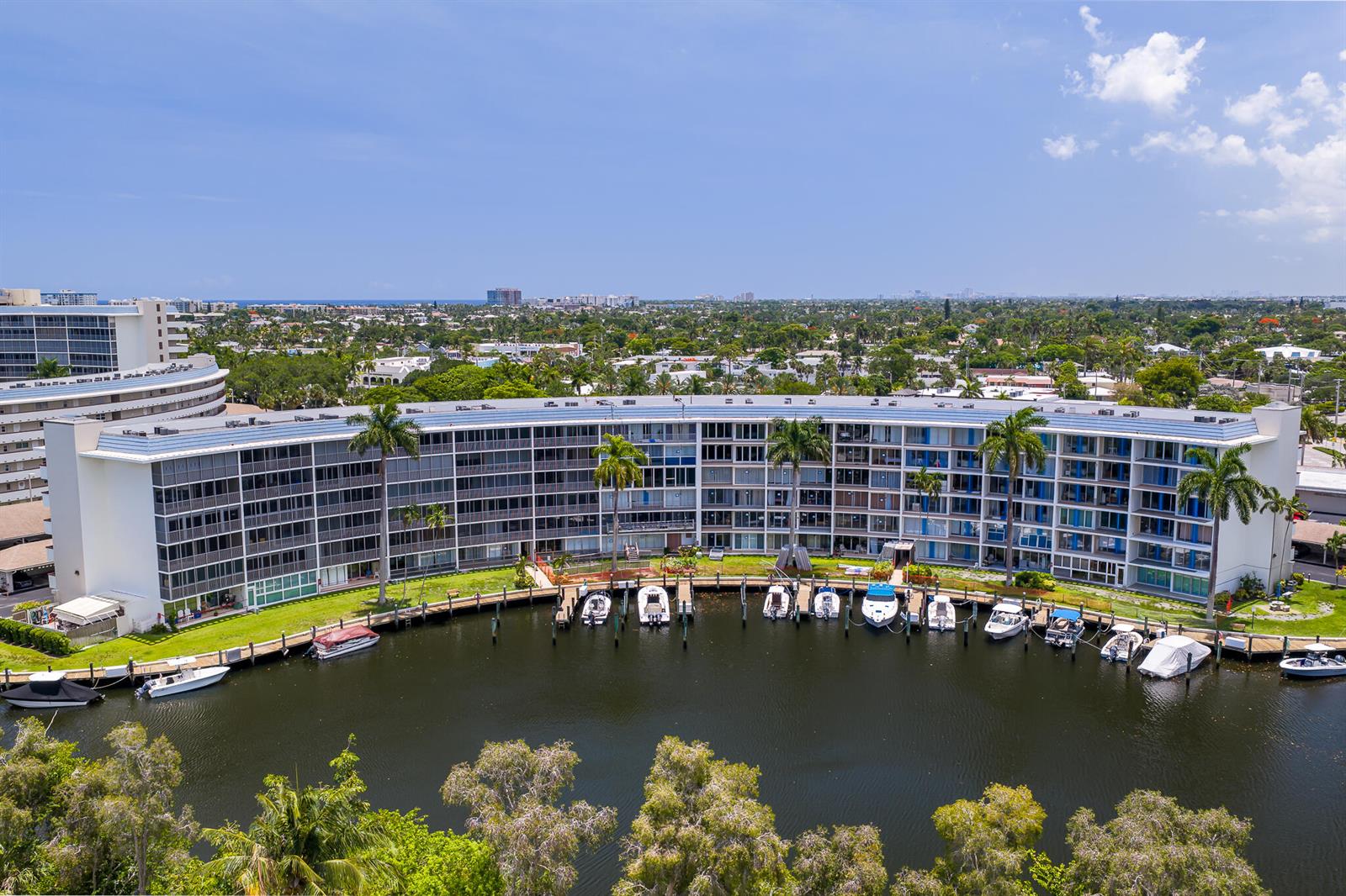 An aerial view shows a curved apartment building with a private boat dock and canal — 1319 E Hillsboro Boulevard # 208, Deerfield Beach FL 33441, DEERFIELD BEACH, FL