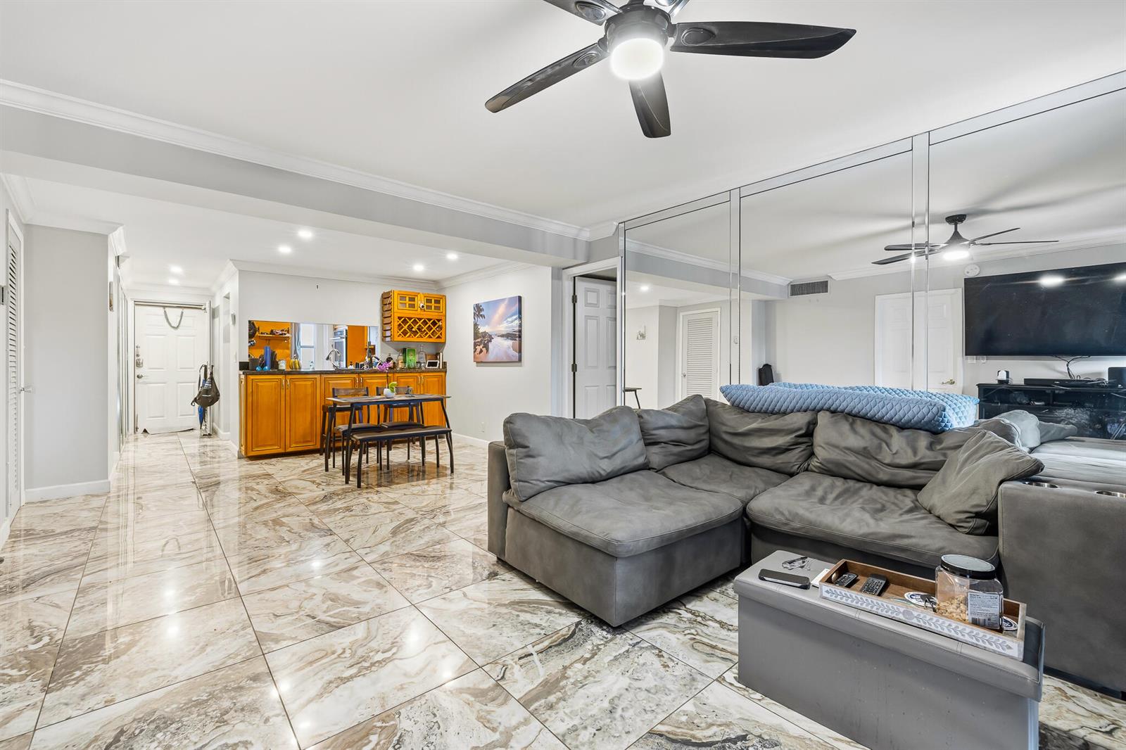 A living room features marble-look tile flooring, a gray sectional sofa, and a mirrored wall — 1319 E Hillsboro Boulevard # 208, Deerfield Beach FL 33441, DEERFIELD BEACH, FL