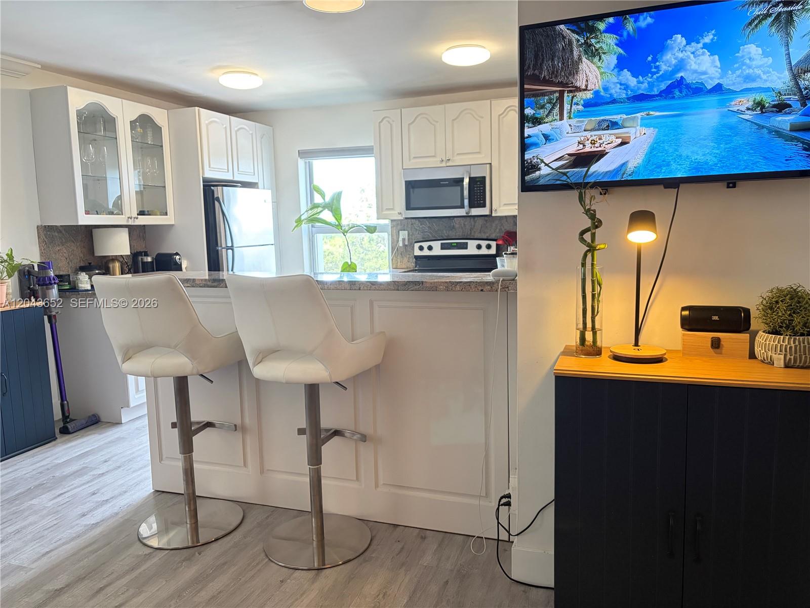 A kitchen features white cabinetry, a granite breakfast bar with two stools, and stainless appliances — 820 Salzedo St # 405, Coral Gables FL 33134, CORAL GABLES, FL