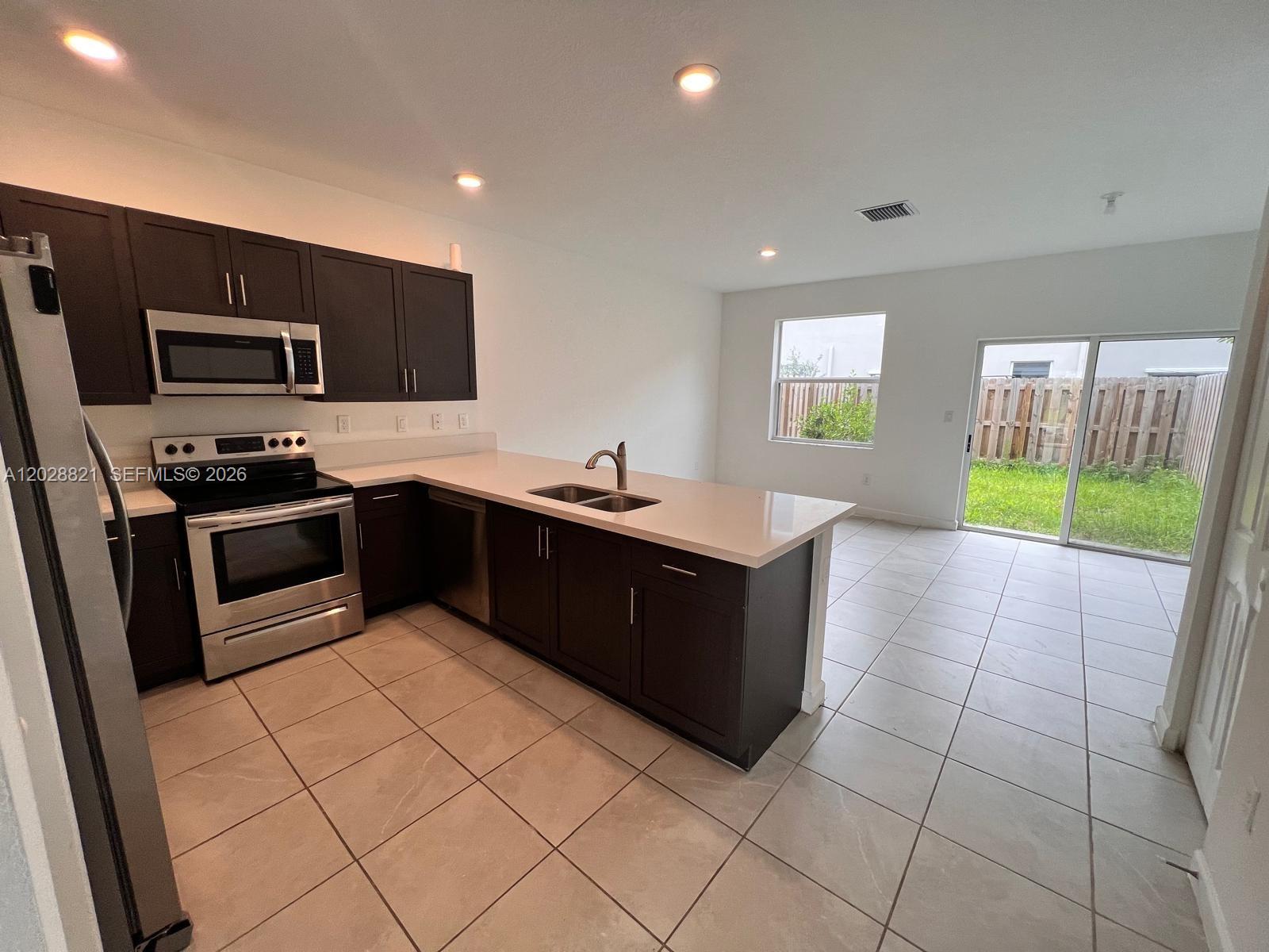 A kitchen with dark cabinets, stainless steel appliances, and a quartz island overlooks a backyard — 1030 SE 26th Ter, Homestead FL 33035, HOMESTEAD, FL