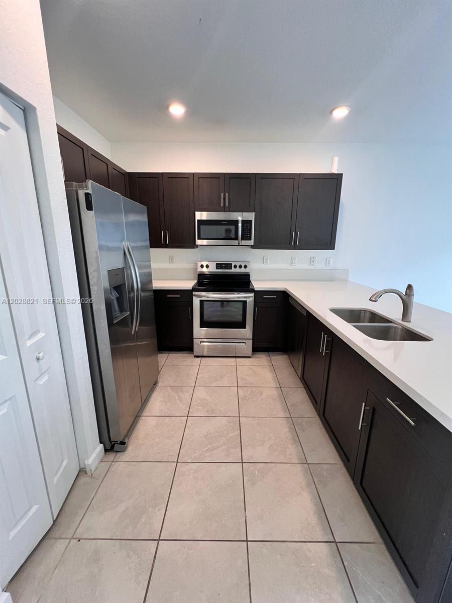 A kitchen features dark wood cabinets, stainless steel appliances, and white countertops — 1030 SE 26th Ter, Homestead FL 33035, HOMESTEAD, FL