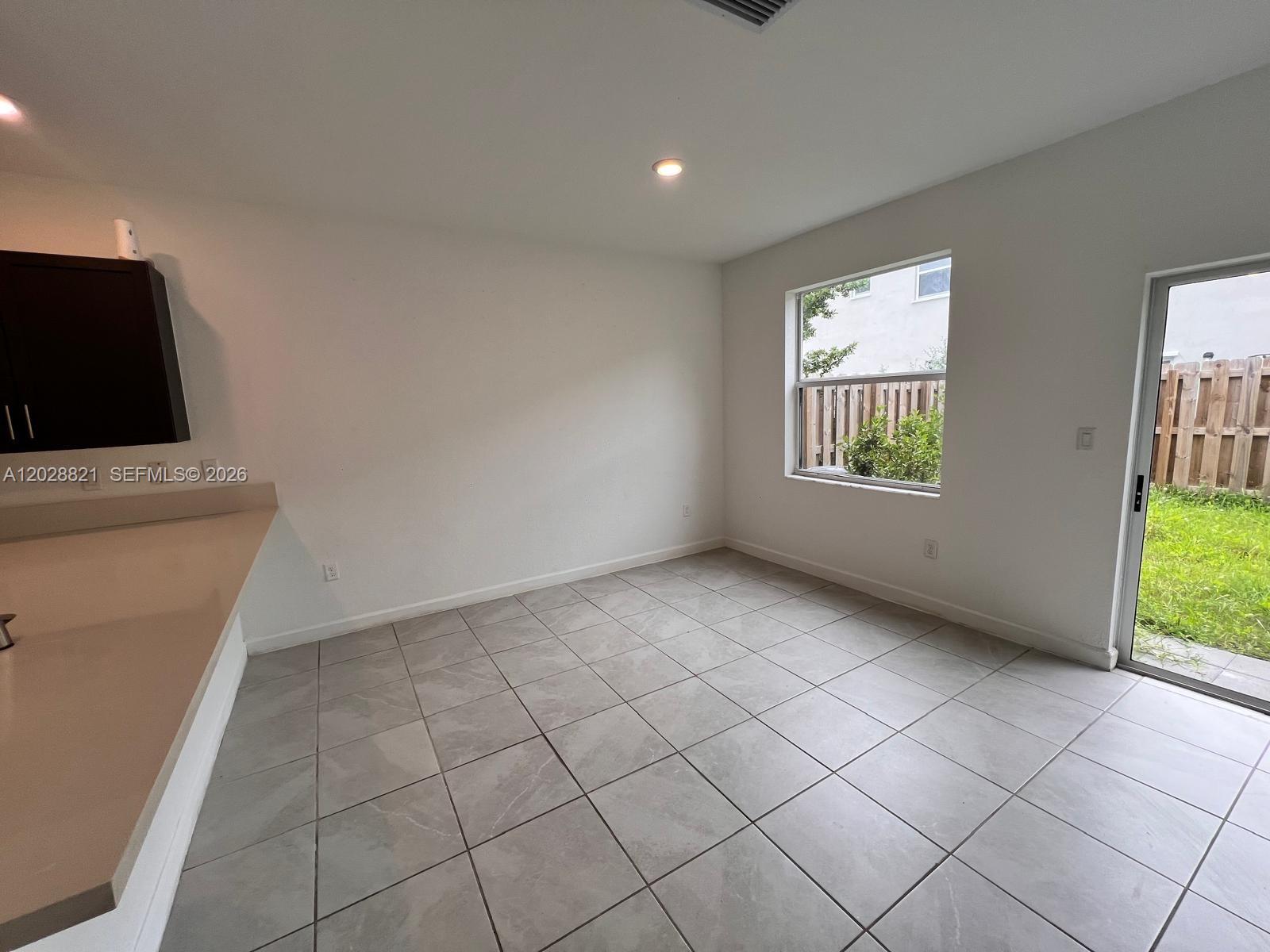 A bright room with light gray tile flooring, a window, and a sliding glass door — 1030 SE 26th Ter, Homestead FL 33035, HOMESTEAD, FL