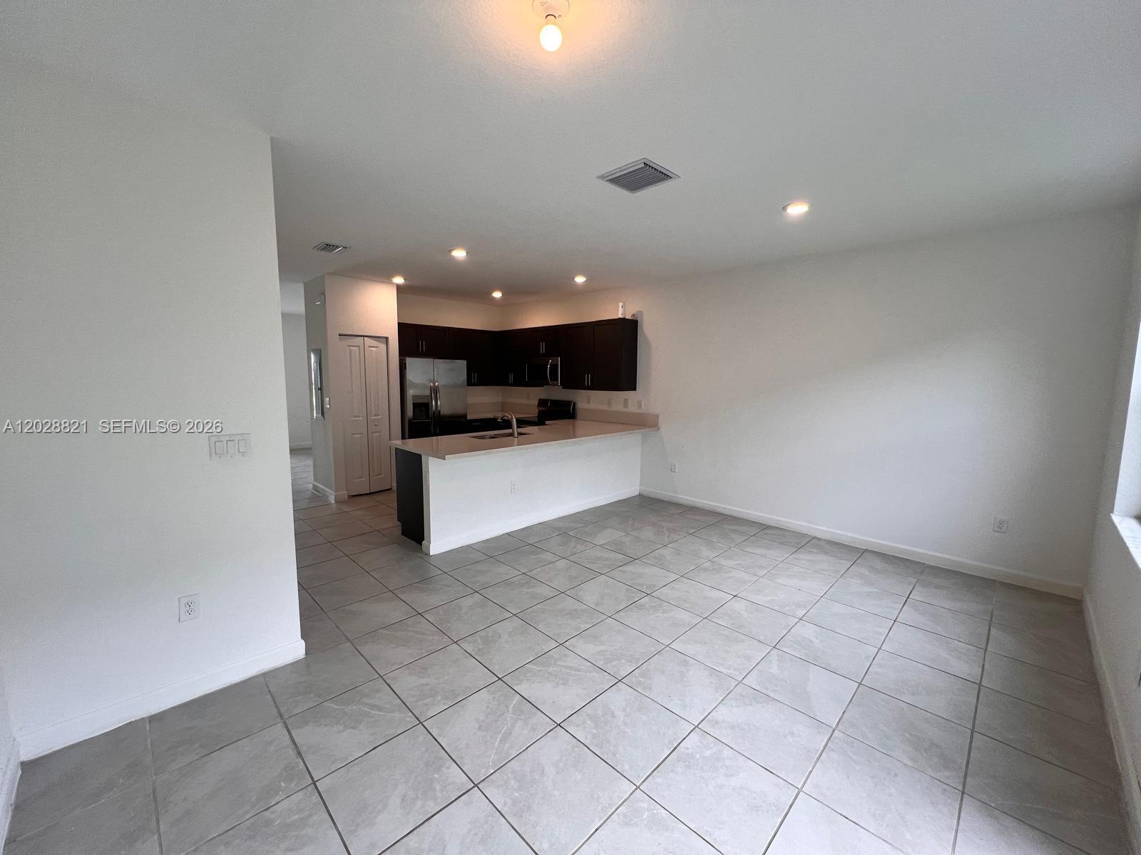 An open-concept kitchen features dark cabinets, light countertops, and gray tile flooring — 1030 SE 26th Ter, Homestead FL 33035, HOMESTEAD, FL