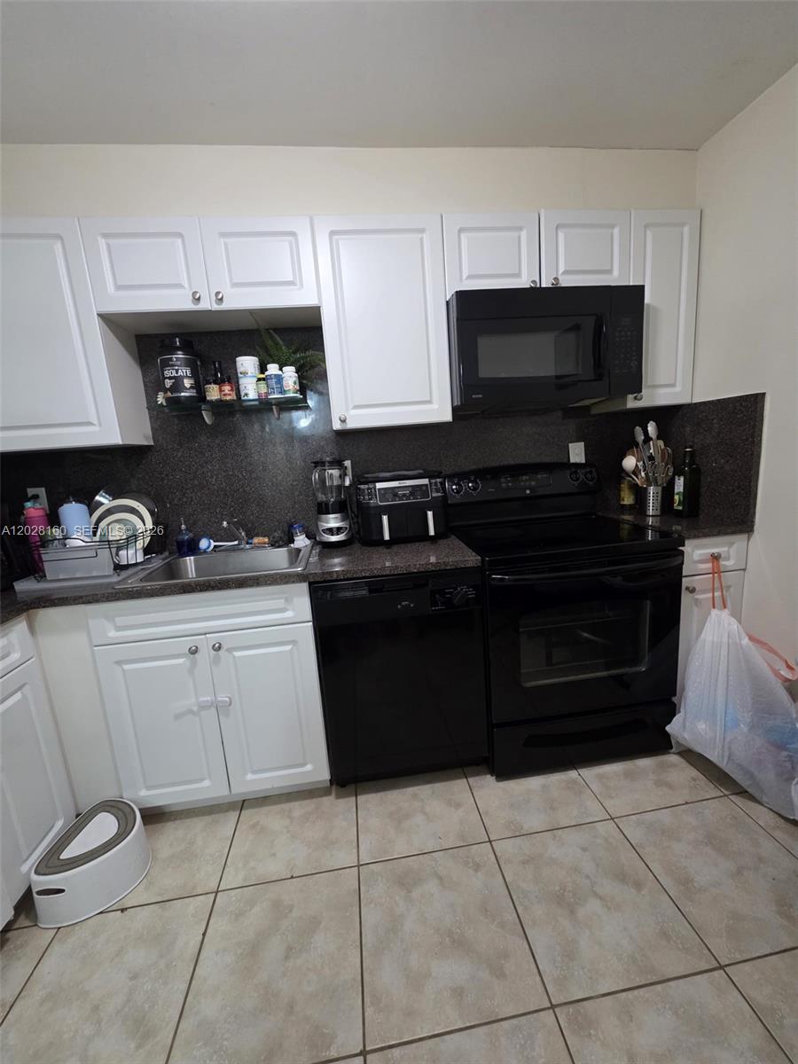 A kitchen features white cabinets, black appliances, a dark countertop, and tiled flooring — 450 Commodore Dr # 108, Plantation FL 33325, PLANTATION, FL