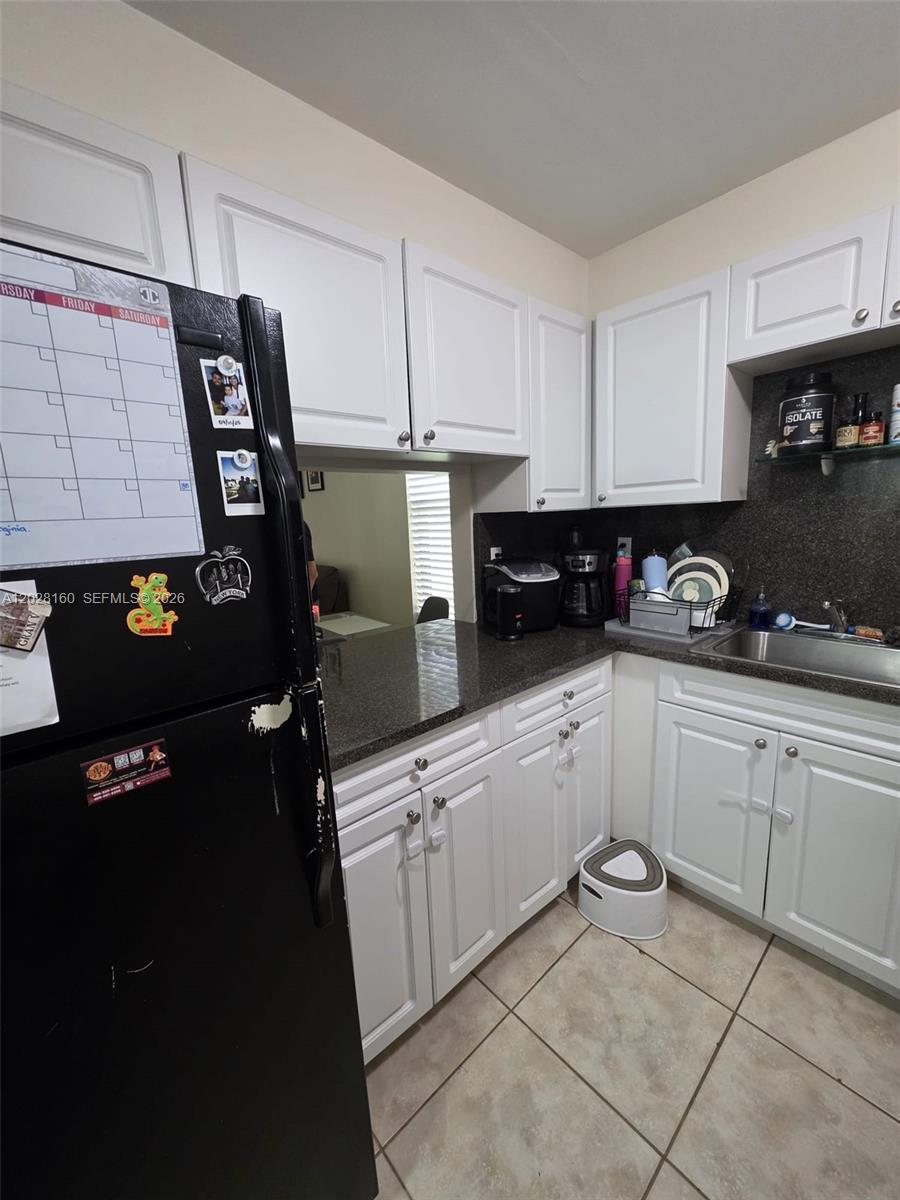 A kitchen features white cabinets, dark countertops, a black refrigerator, and tile flooring — 450 Commodore Dr # 108, Plantation FL 33325, PLANTATION, FL