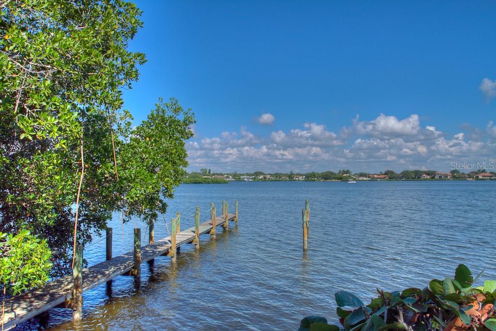 A wooden dock extends into a calm bay surrounded by trees and distant houses — 3434 CASEY KEY ROAD, NOKOMIS, FL