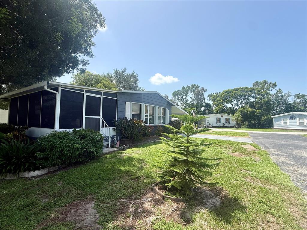 A blue manufactured home features a screened-in porch and a small pine tree in front — 9735 LAKE FAIRWAYS BOULEVARD, NORTH FORT MYERS, FL
