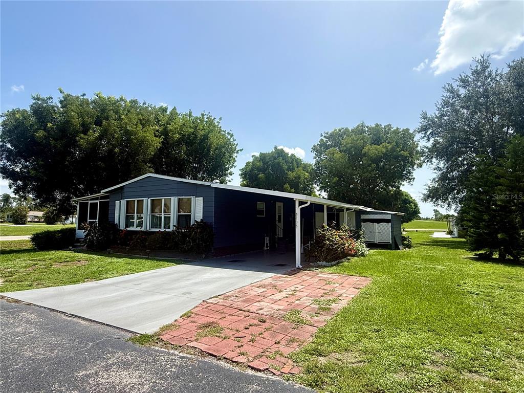 A blue single-story house with a carport and a brick-paved driveway sits on a lawn — 9735 LAKE FAIRWAYS BOULEVARD, NORTH FORT MYERS, FL
