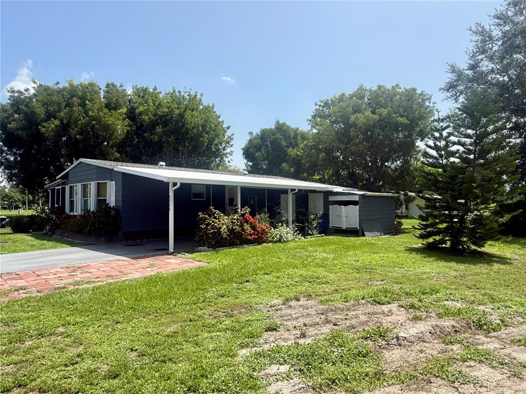 A single-story house with blue siding, a white carport, and a large front lawn — 9735 LAKE FAIRWAYS BOULEVARD, NORTH FORT MYERS, FL
