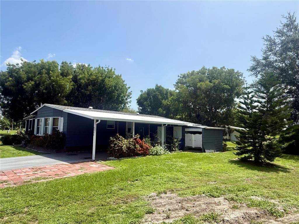 A dark-sided house features a covered patio, landscaping, and a white lattice privacy screen — 9735 LAKE FAIRWAYS BOULEVARD, NORTH FORT MYERS, FL