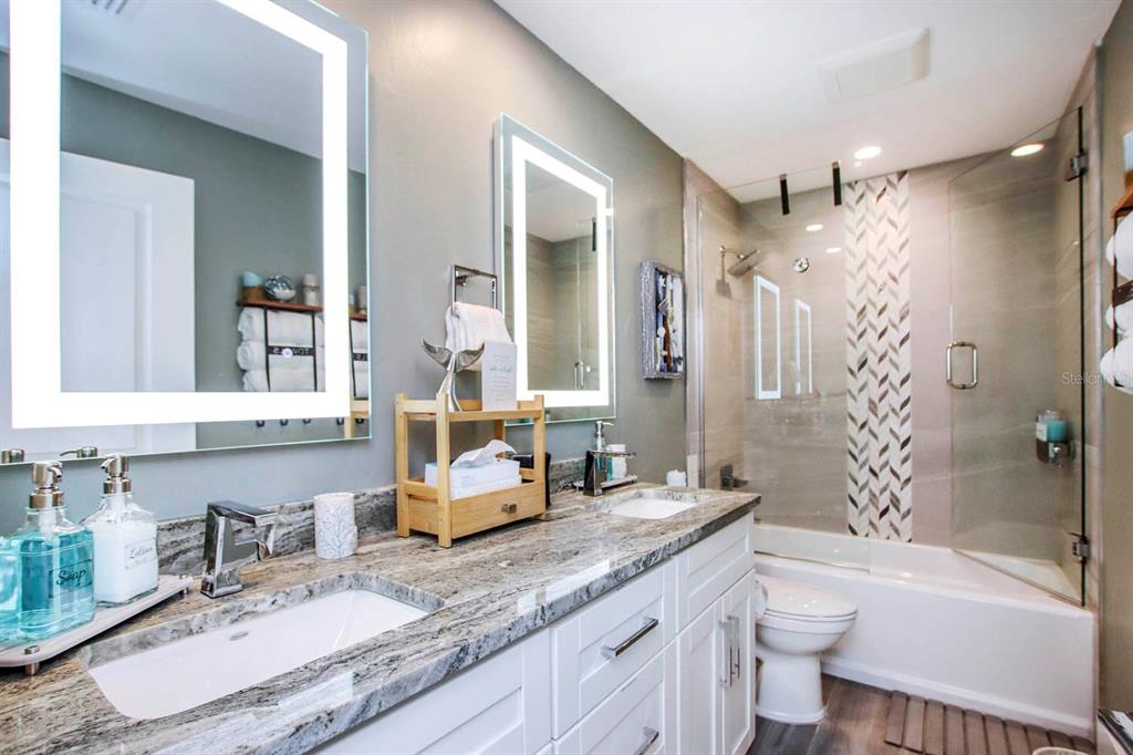 A bathroom with a double vanity, granite countertops, two lighted mirrors, and a glass-enclosed shower — 3328 SE 18TH AVENUE, CAPE CORAL, FL