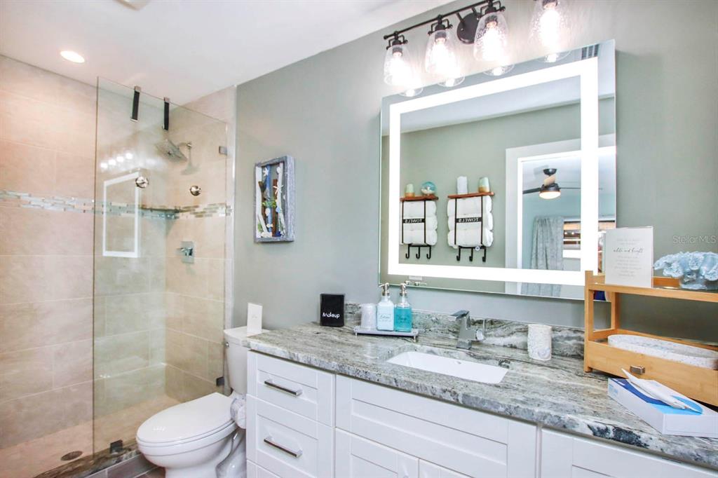 A bathroom features a granite vanity, a lighted mirror, and a glass-enclosed walk-in shower — 3328 SE 18TH AVENUE, CAPE CORAL, FL