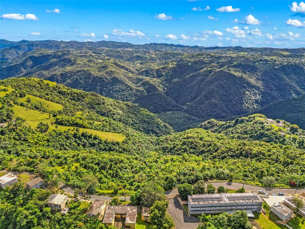 An aerial view shows a multi-story building nestled in a lush, mountainous landscape — Carr 156 Km 20.1 INTERIOR BO HONDURAS, BARRANQUITAS, PR