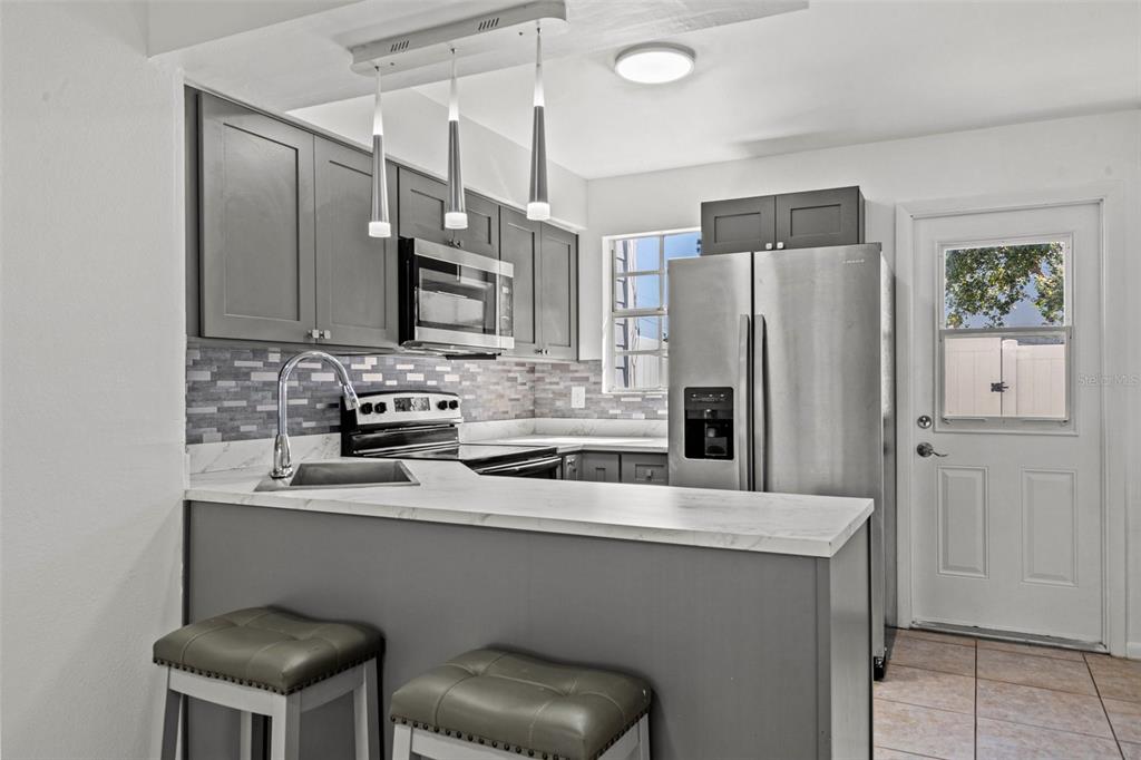 A kitchen features gray cabinets, stainless steel appliances, a breakfast bar, and tile flooring — 6650 121ST AVENUE UNIT 4, LARGO, FL