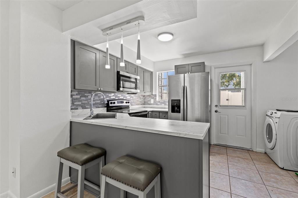 A kitchen features gray cabinets, stainless steel appliances, a breakfast bar, and tile flooring — 6650 121ST AVENUE UNIT 4, LARGO, FL