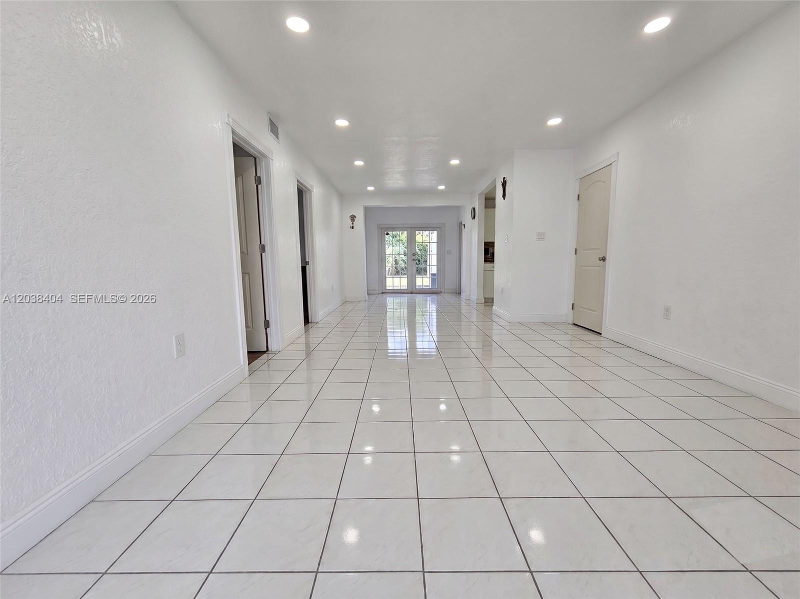 A bright, empty hallway features white walls, recessed lighting, and large white floor tiles — HIALEAH, FL