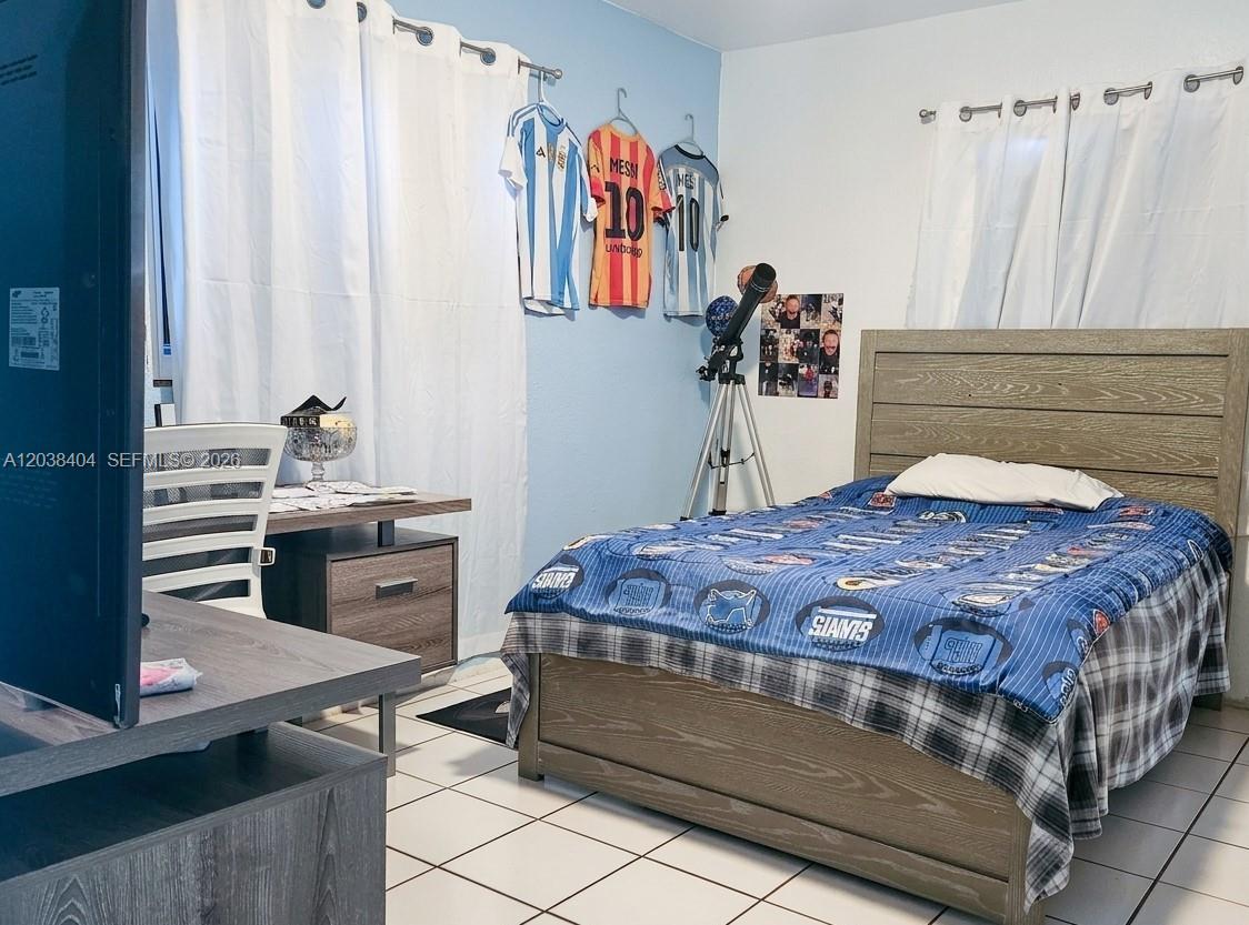 A bedroom features a bed with a blue patterned comforter, a desk, and soccer jerseys — HIALEAH, FL